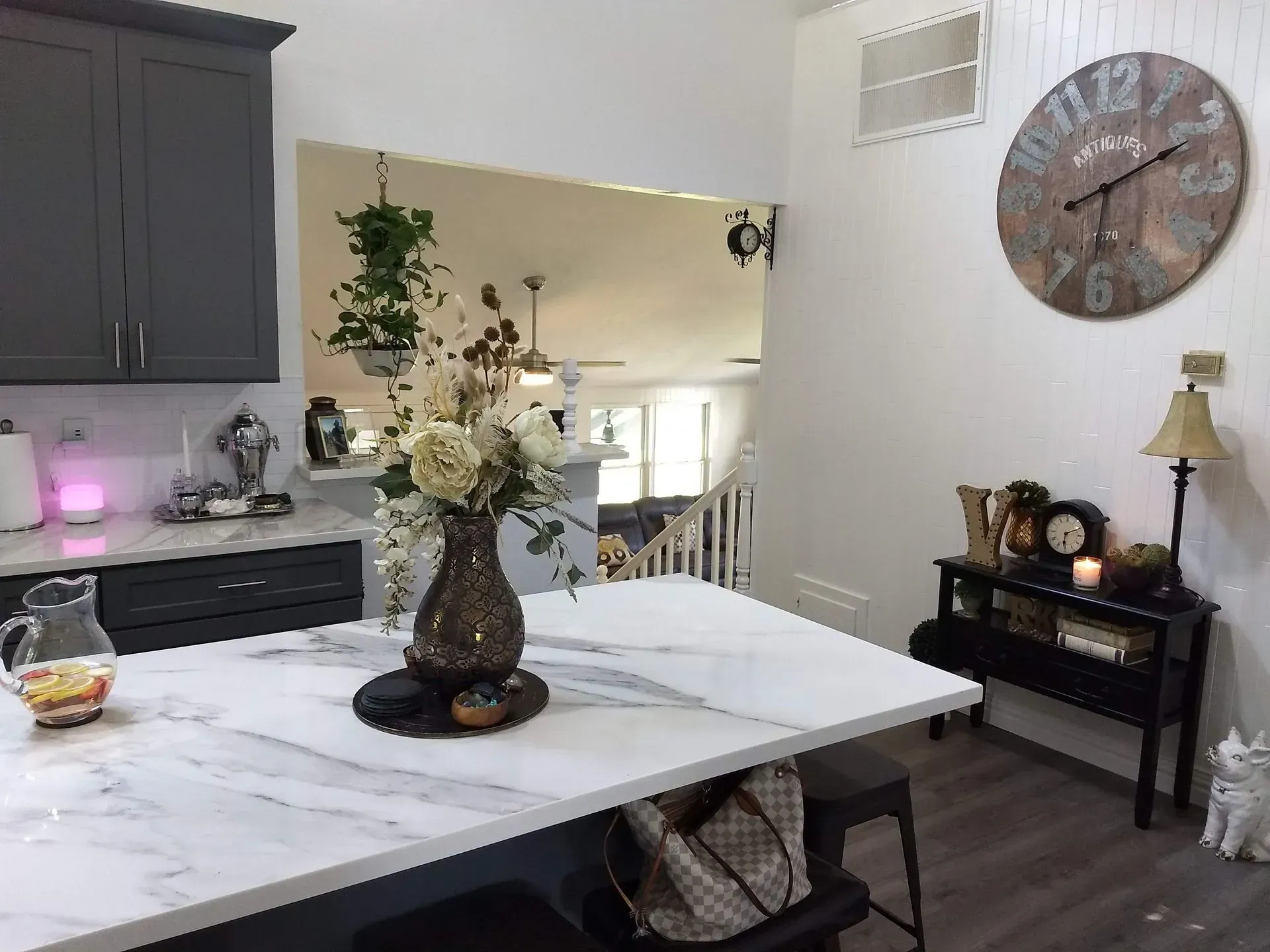 Modern kitchen with marble island, floral centerpiece, gray cabinets, and wall clock