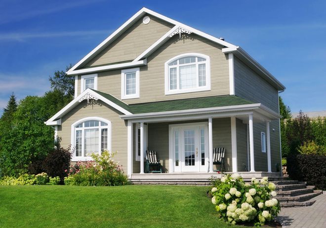Two-story gray house with white trim, front porch, and green lawn under a blue sky