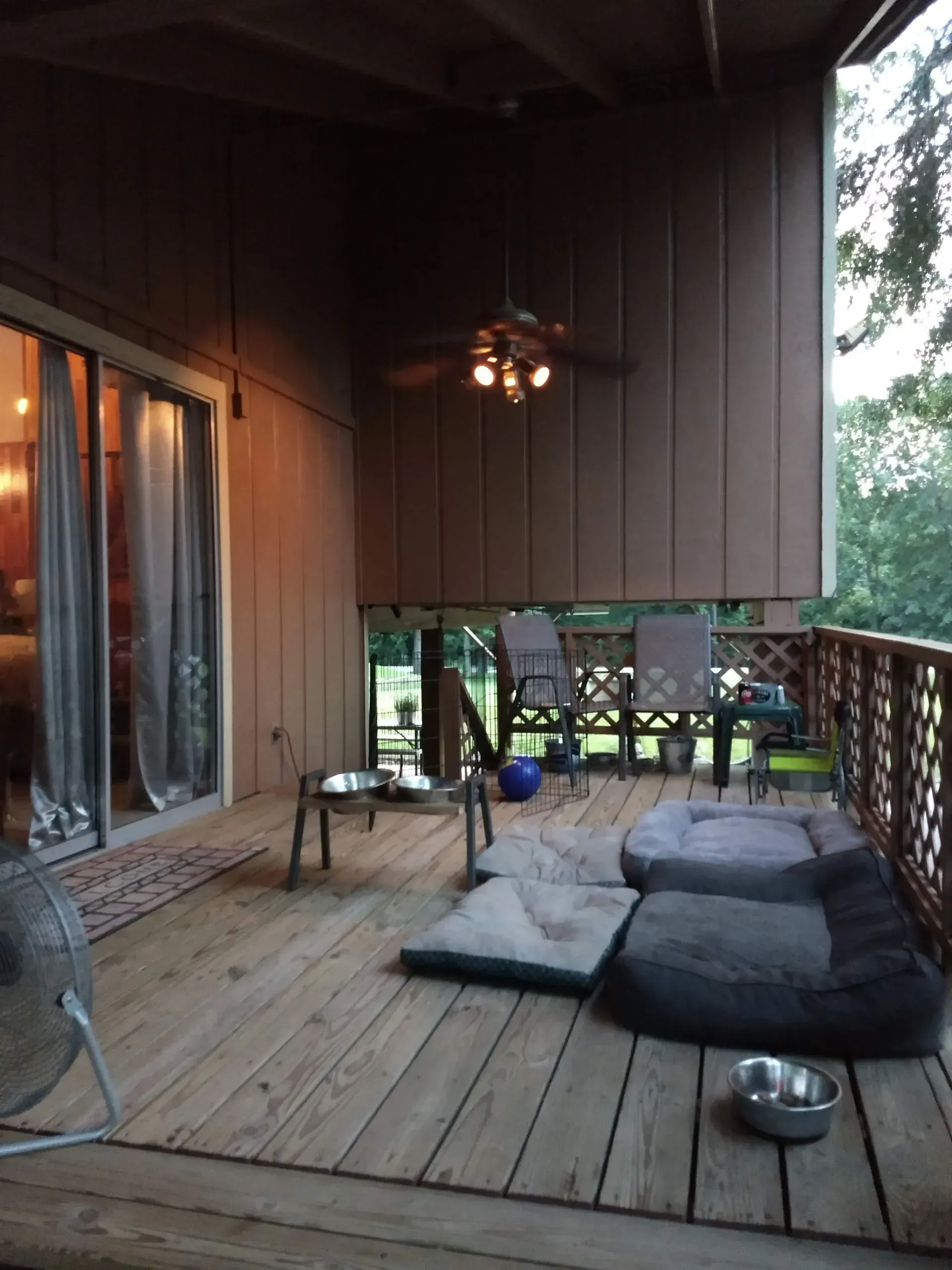 Wooden deck patio with cushions, sliding glass doors, and trees visible beyond the railing.