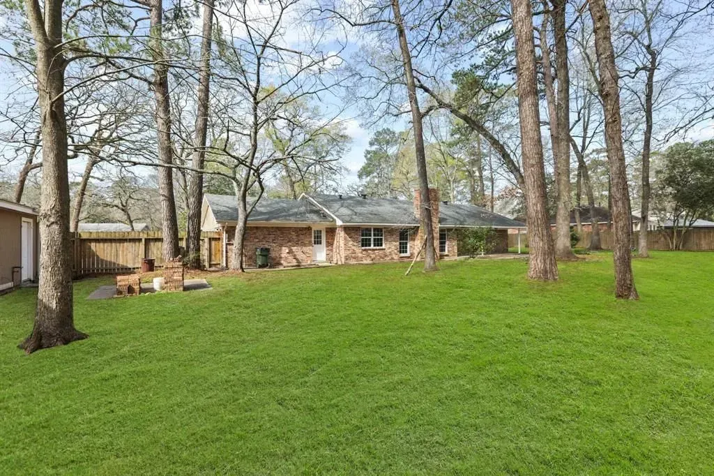 Wide grassy backyard with tall leafless trees and a single-story house in the background