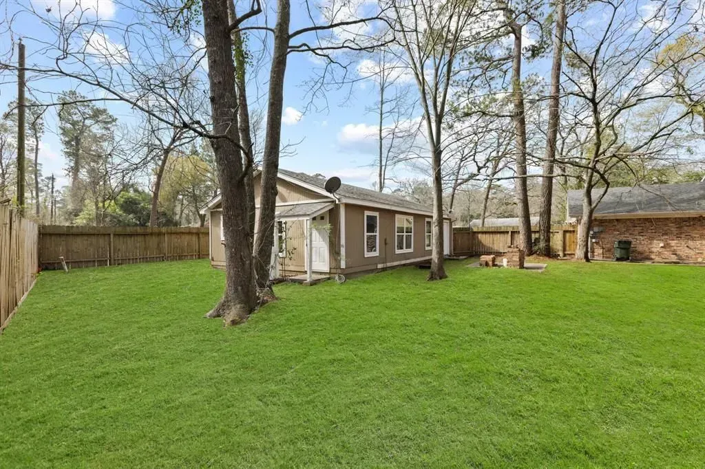 Backyard with green lawn, tall trees, and a small beige shed under a partly cloudy sky