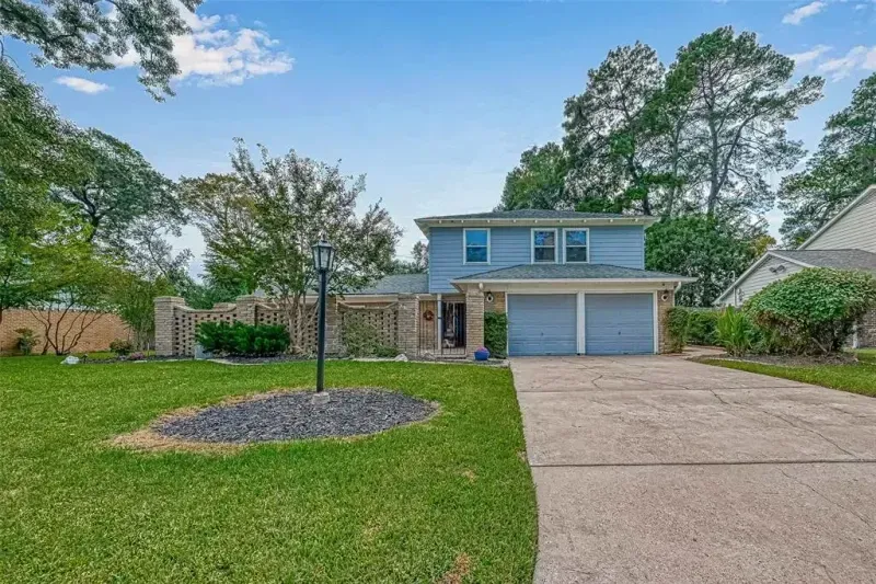 Two-story blue house with attached garage, wide driveway, and front lawn under a partly cloudy sky