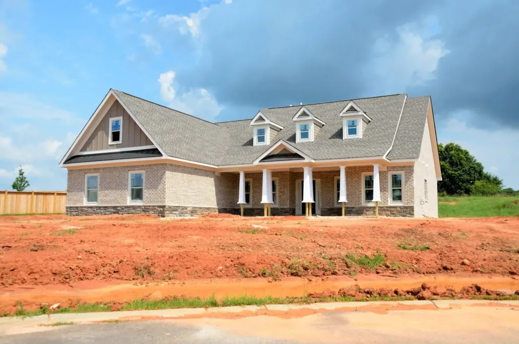 New house with gray roof and brick exterior on a red dirt lot under a blue sky