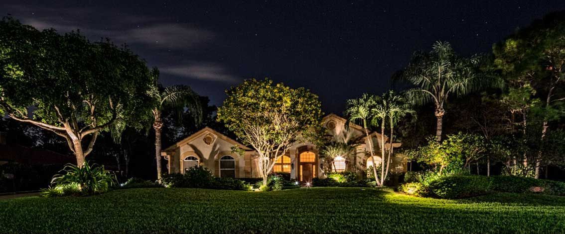 A well-lit house at night with trees and a dark sky filled with stars.