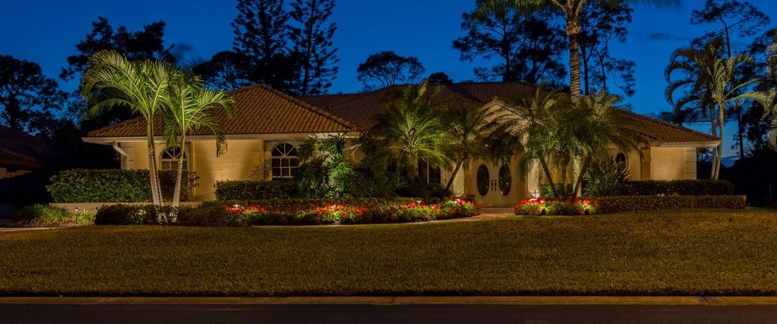 House at night with outdoor lighting illuminating the facade, trees, and landscaping.