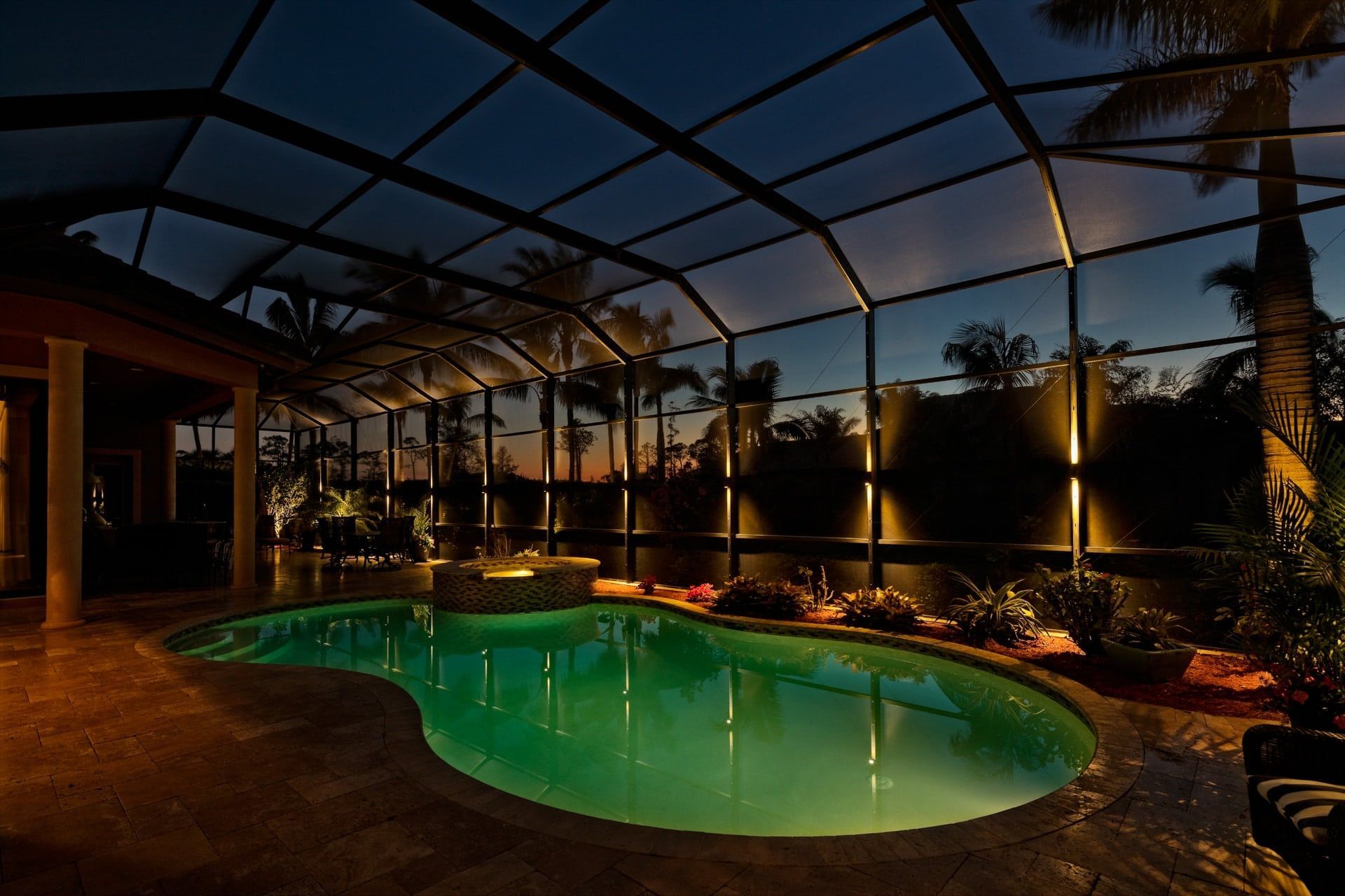 Pool enclosed by screen, illuminated at night with palm trees in the background.