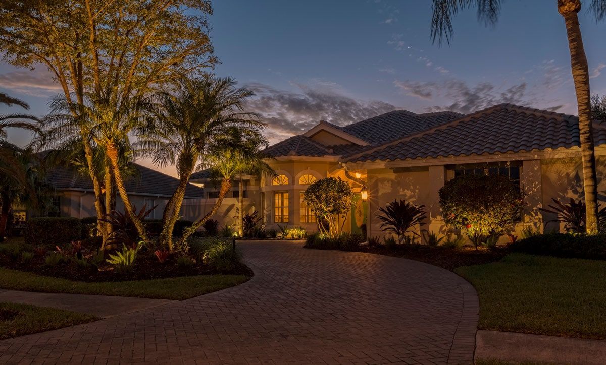 A house at dusk with landscape lighting highlighting the driveway, trees, and front of the home.