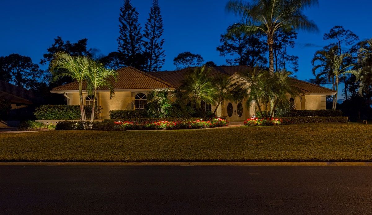 House at dusk with outdoor lighting illuminating palm trees and landscaping.