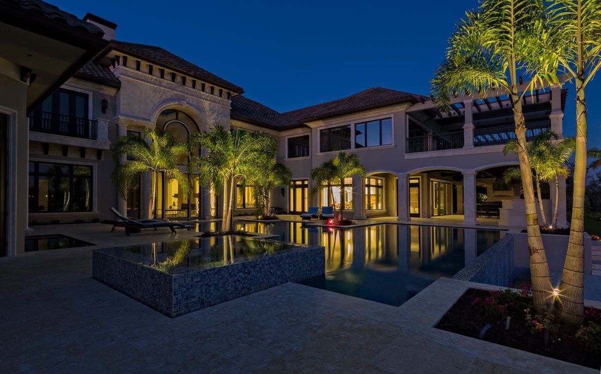 Luxury mansion exterior at night with illuminated pool and palm trees.