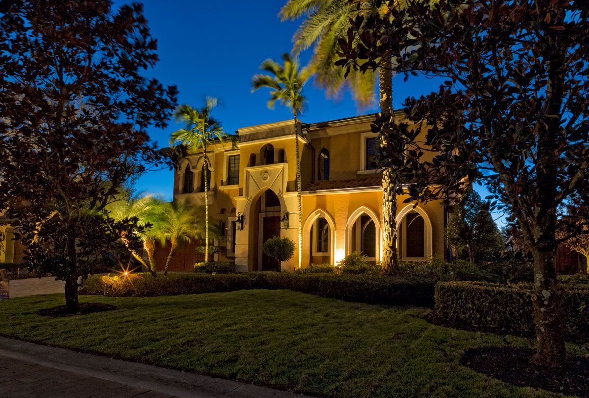 A two-story Mediterranean-style home illuminated at dusk with palm trees and manicured lawn.