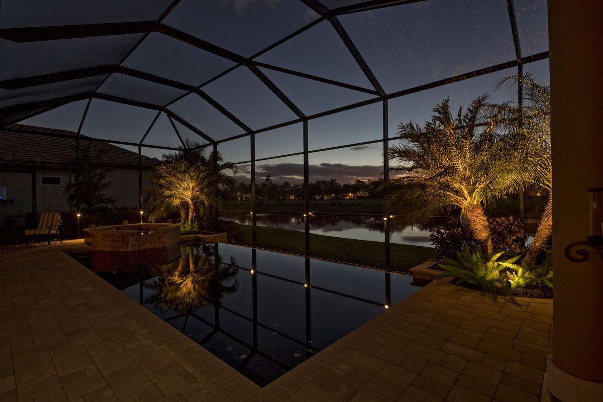 Night view of a pool enclosed in a screen with landscape lighting reflecting on the water.