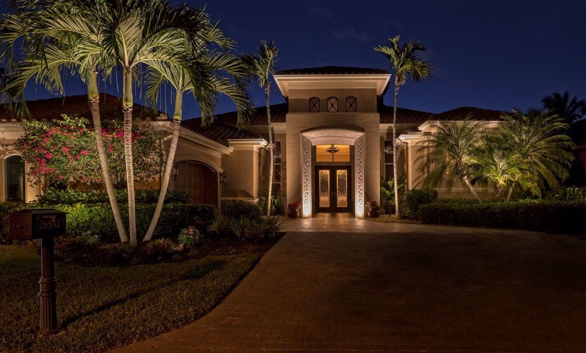 Luxury home illuminated at night with palm trees and a long driveway.