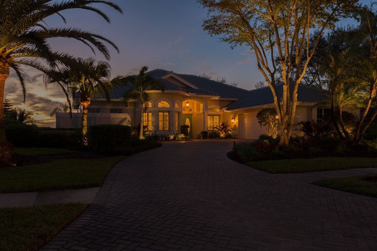 Illuminated house at dusk, driveway leading to the front door, landscaped yard, warm lighting.