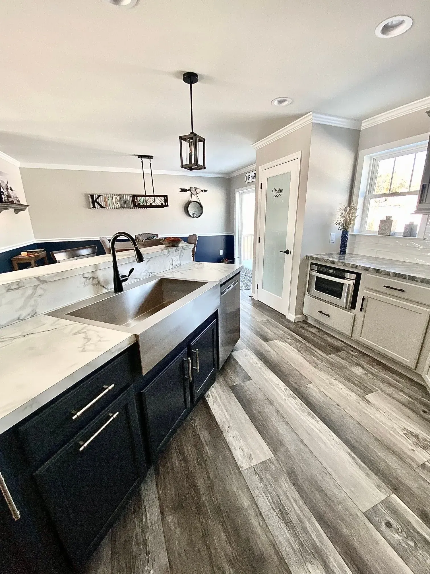 Modern kitchen with white marble countertops, dark blue base cabinets, stainless steel sink, and wood-look laminate floors.