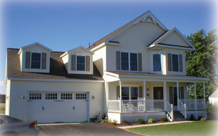 White two-story suburban house with gray shutters, front porch, and landscaped yard under green trees.
