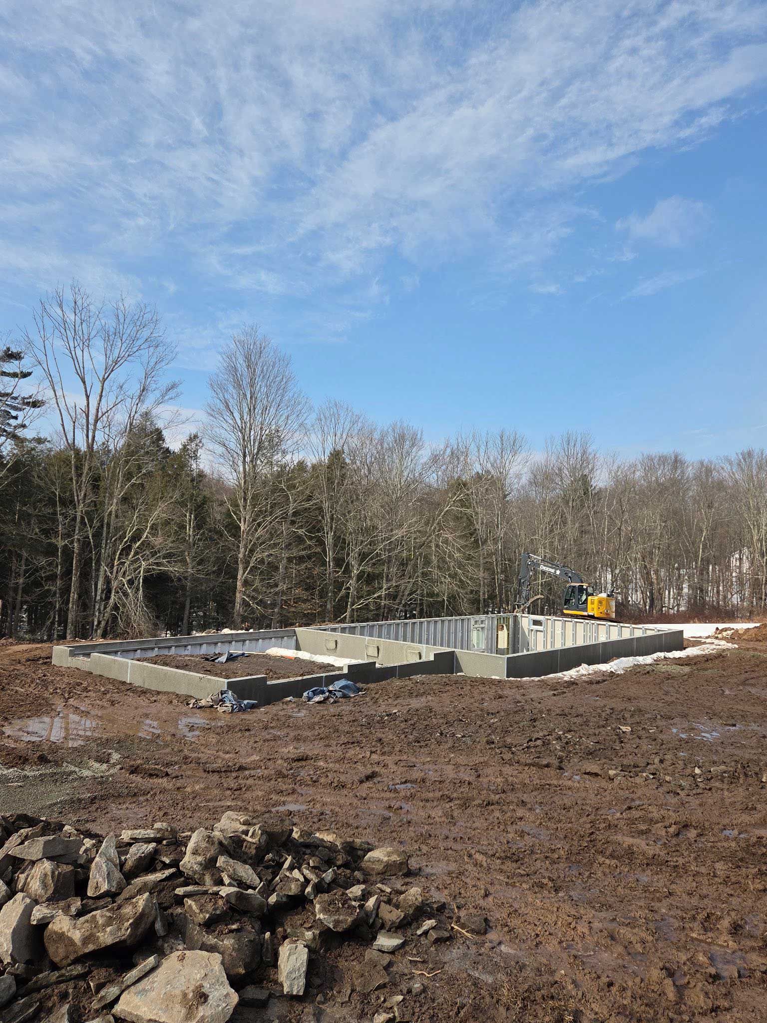 Foundation of a building under construction on muddy ground with trees and blue sky.