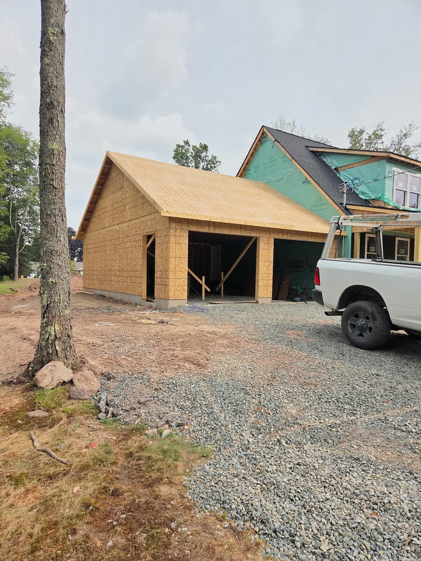 Garage under construction with wooden frame, two bays, and gravel driveway.