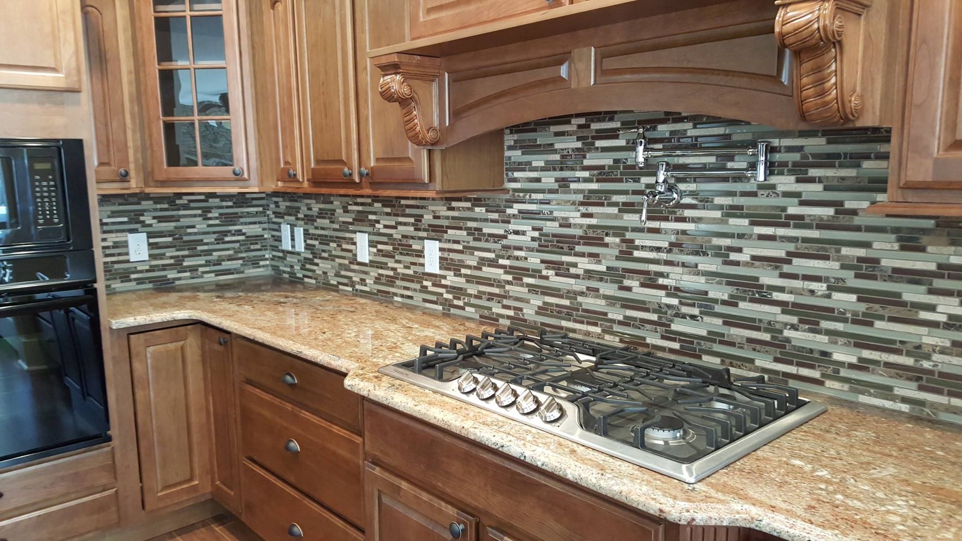 Kitchen with brown cabinets, granite countertops, and mosaic tile backsplash above a gas stovetop.