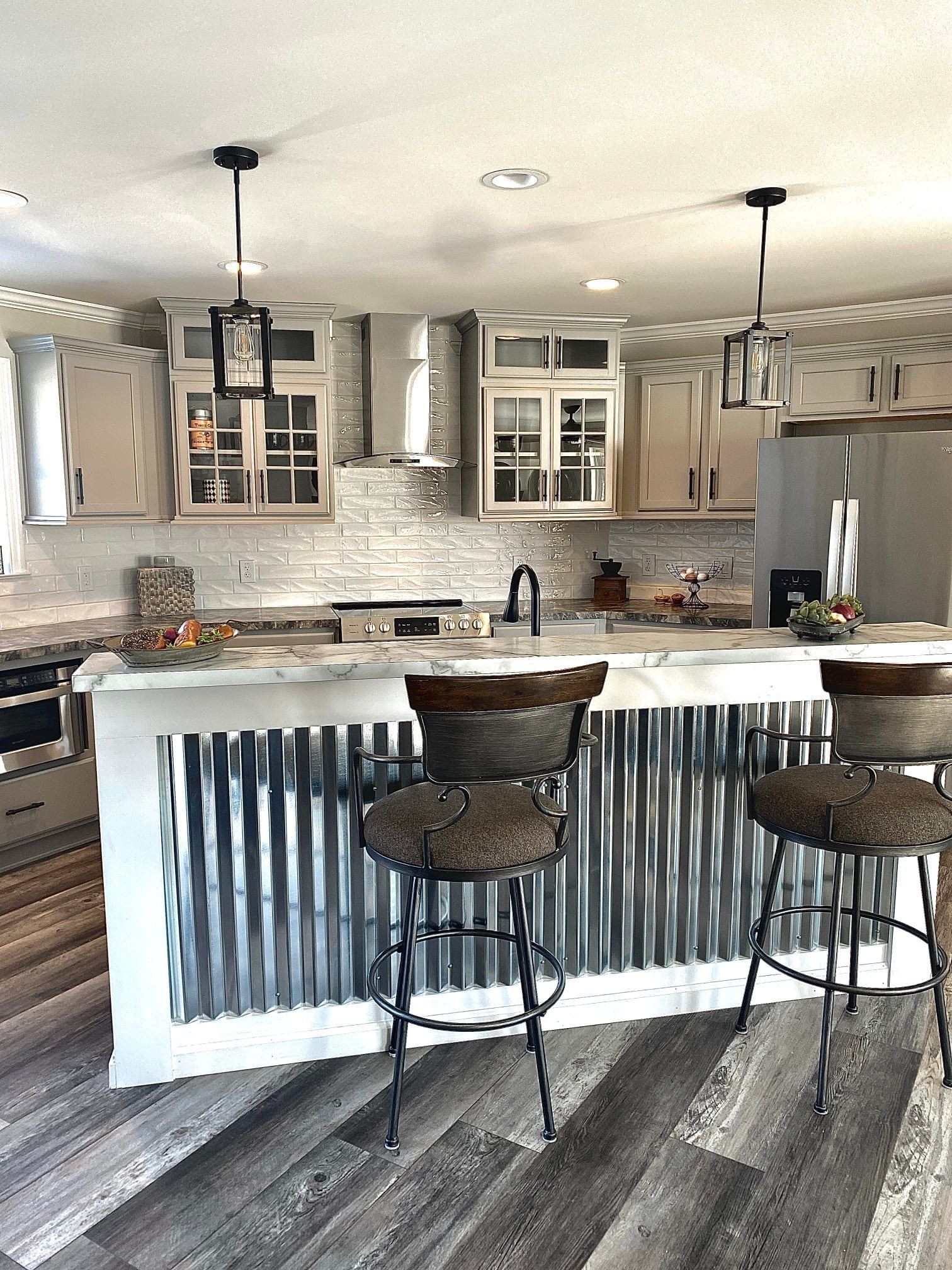 Kitchen with corrugated metal island, cabinets, stools, and pendant lights.