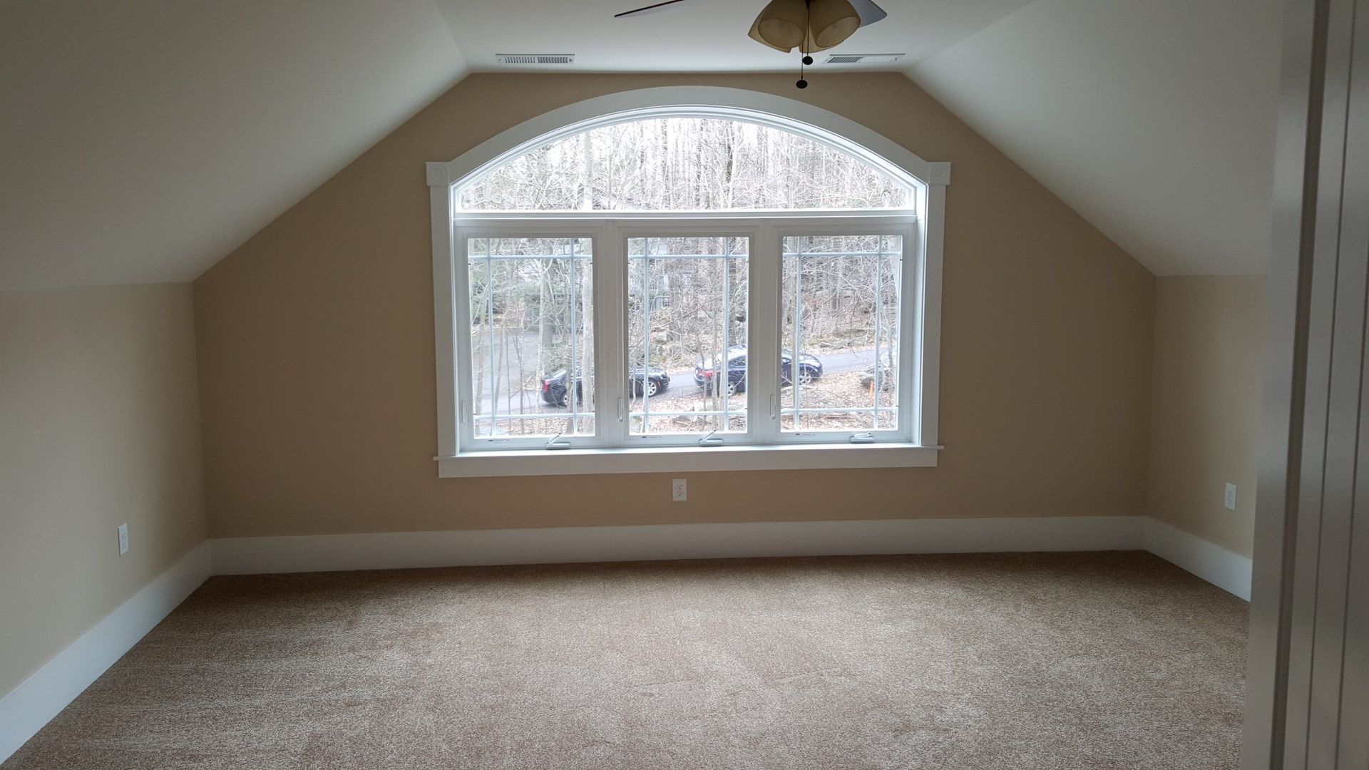 Empty room with tan walls, arched window, and brown carpet.