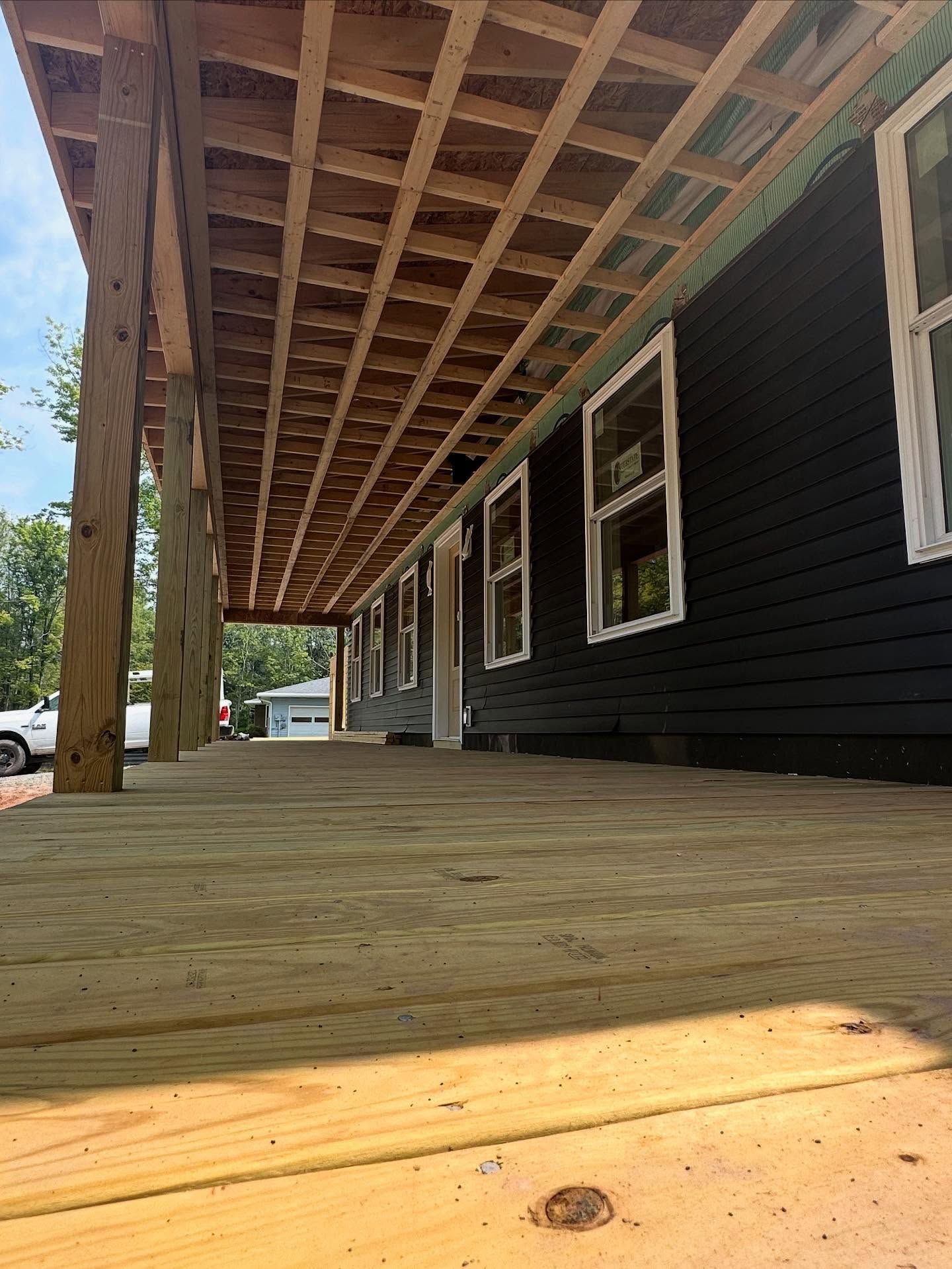 Wooden deck under construction with a black house and white windows.