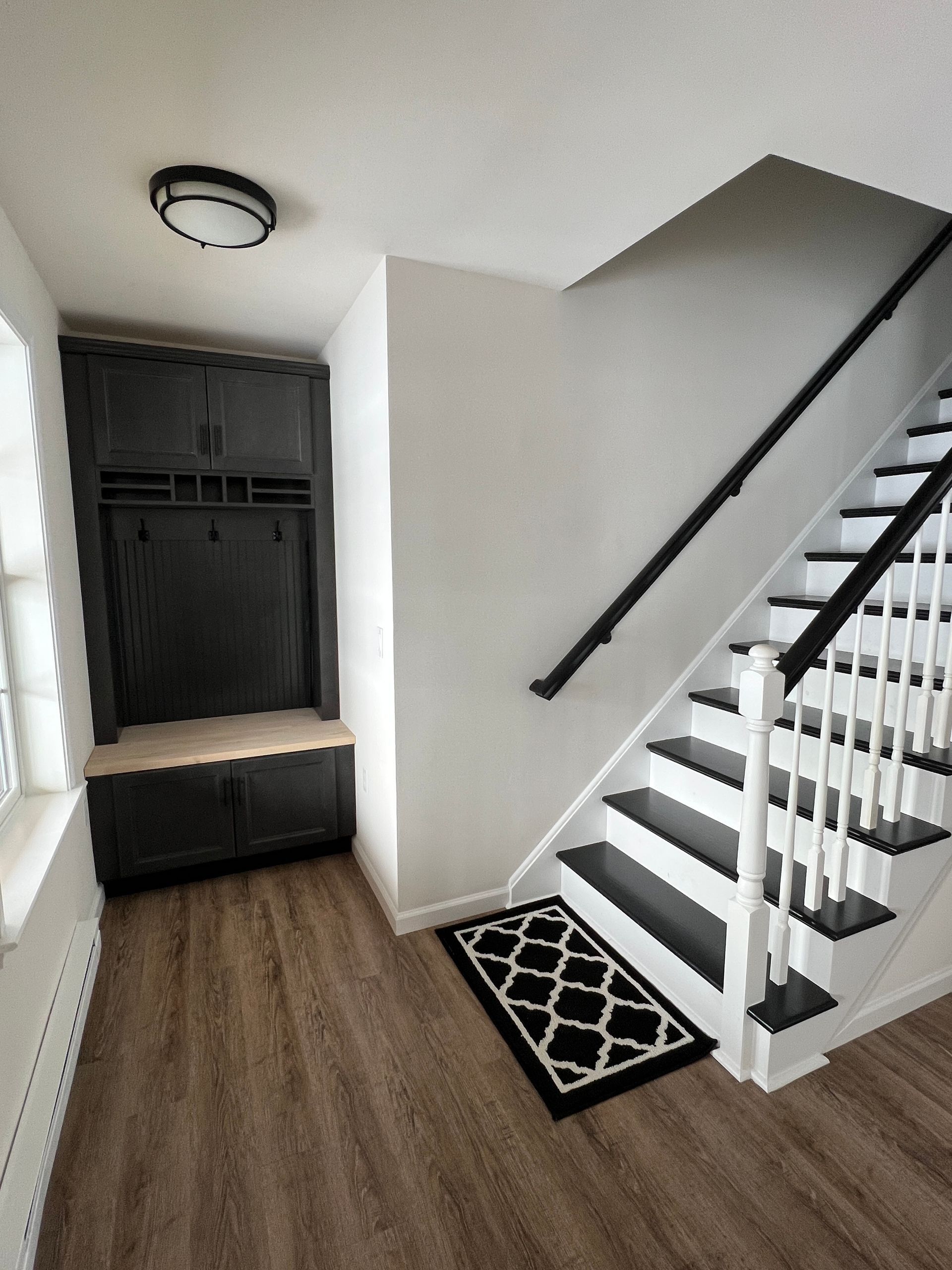 Entryway with black coat rack and staircase. White walls, wood floor, and black and white rug.
