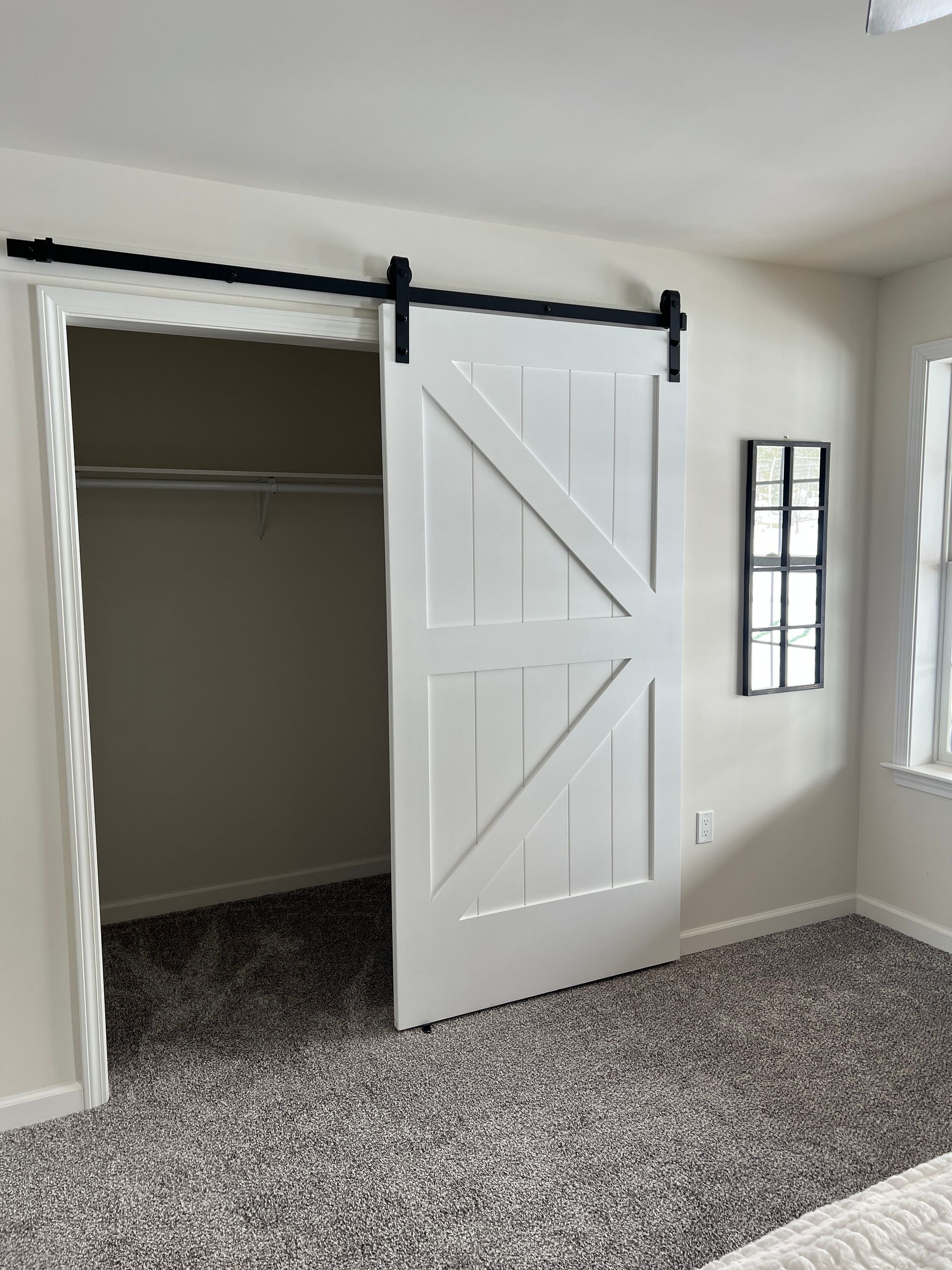 White barn door partially open on a closet. Black hardware, neutral-colored walls, and gray carpet.
