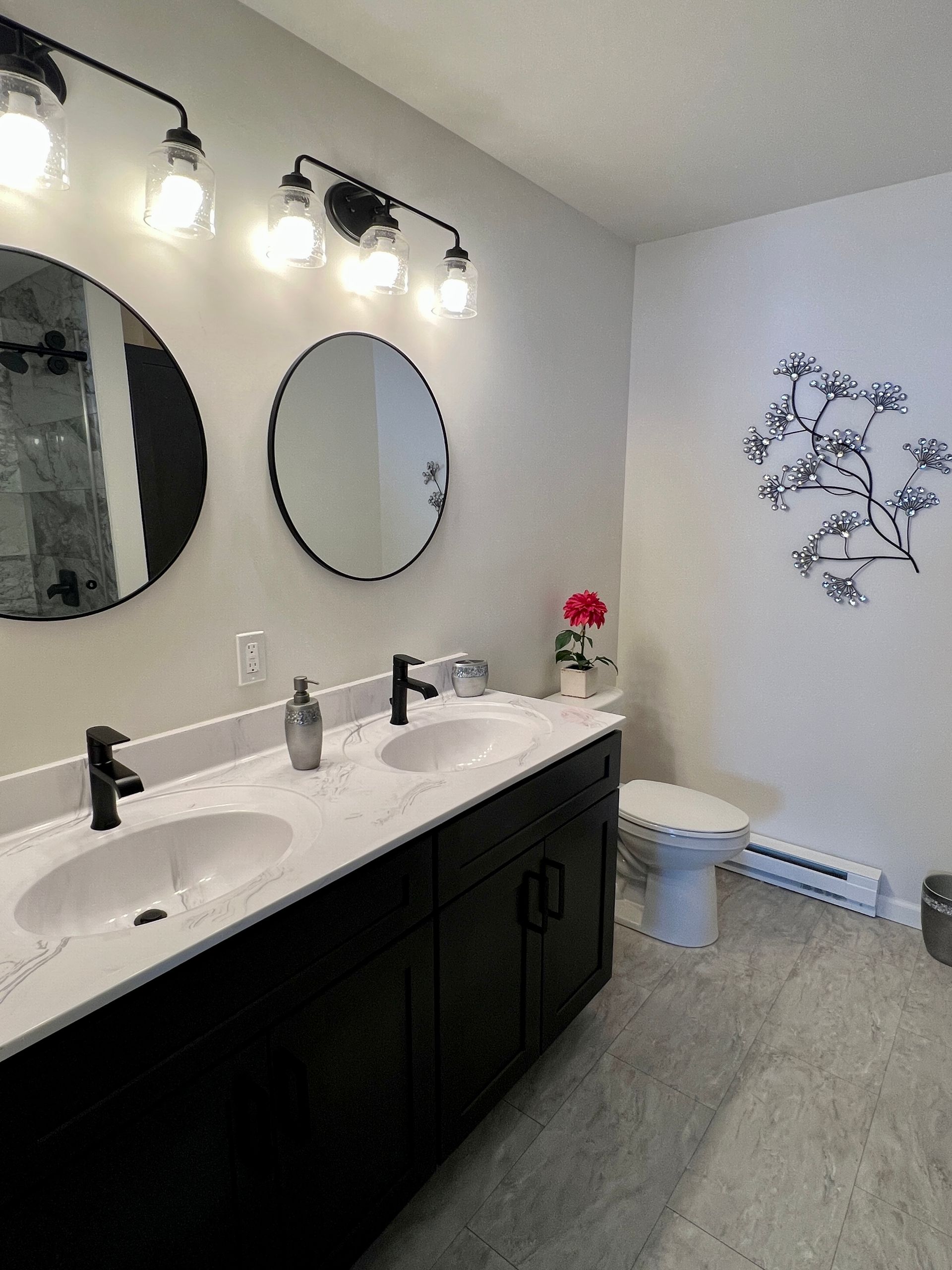 Modern bathroom with black vanity, two sinks, round mirrors, and decorative wall art.