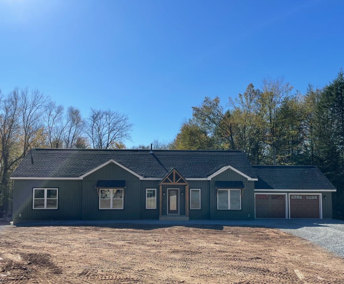 A newly built, one-story house with dark siding, brown garage doors, and a dark roof.
