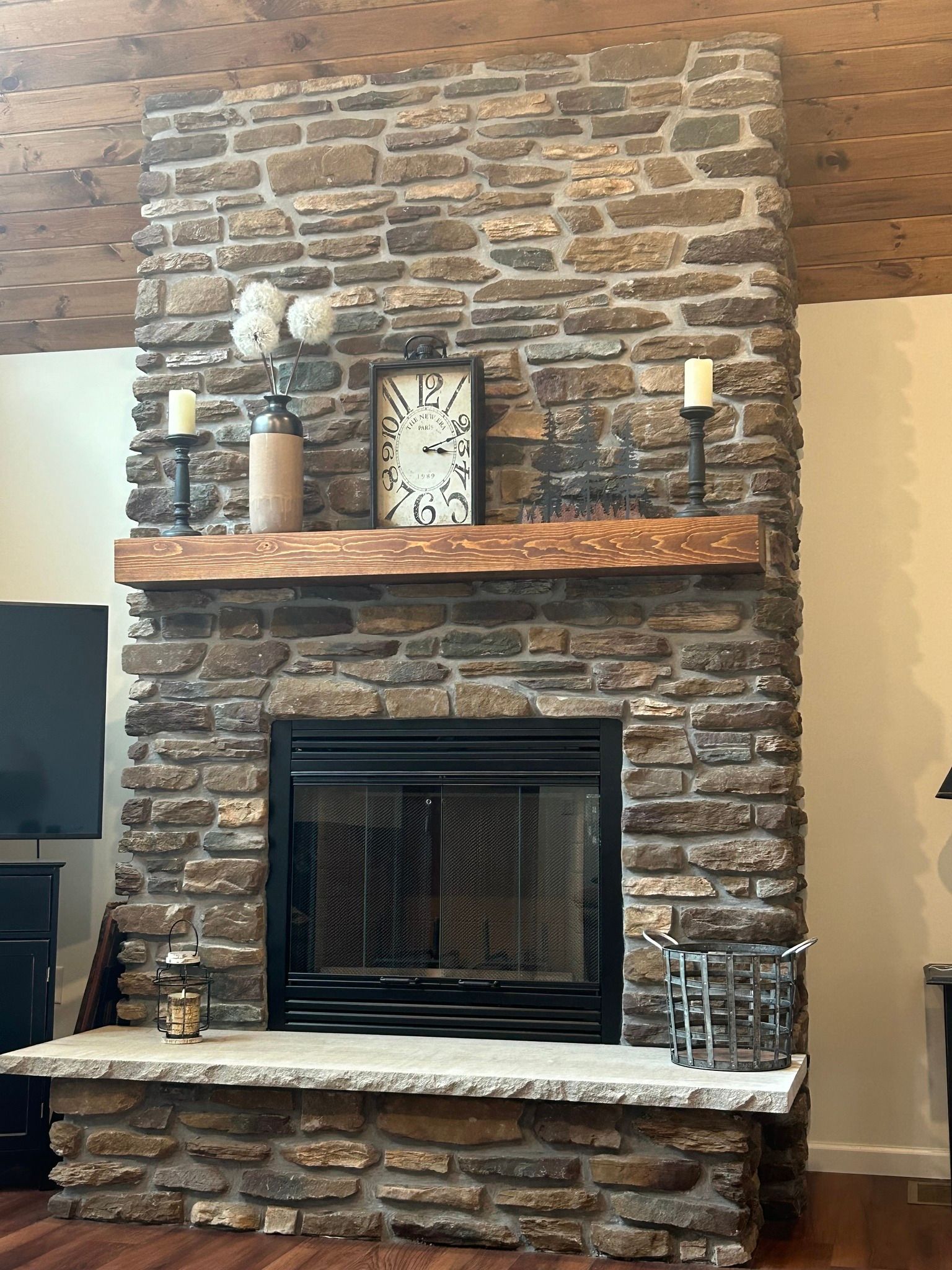 Stone fireplace with wooden mantle, clock, candles, and decor.