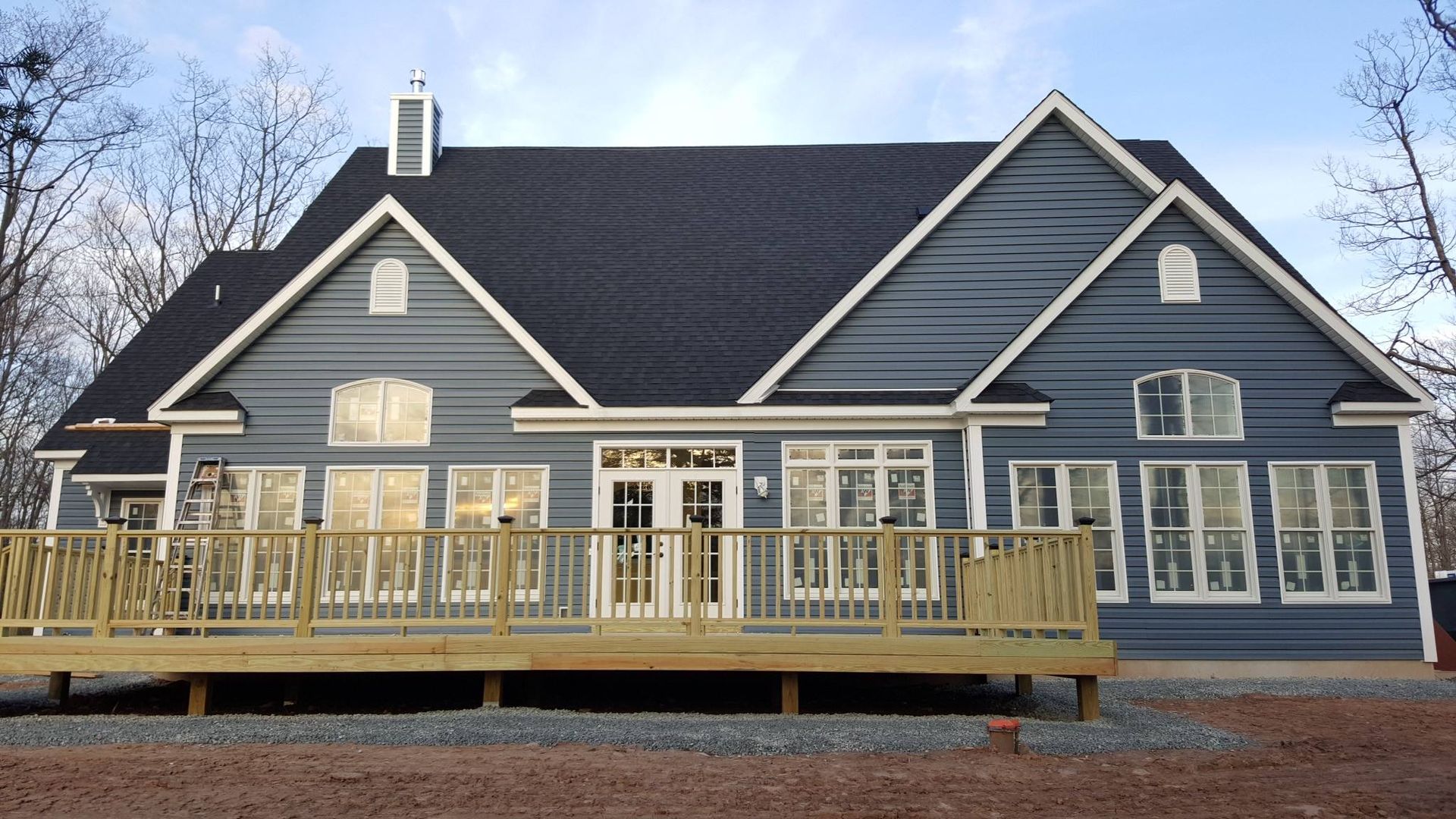 Blue house with a wooden deck, multiple windows, and a black roof.