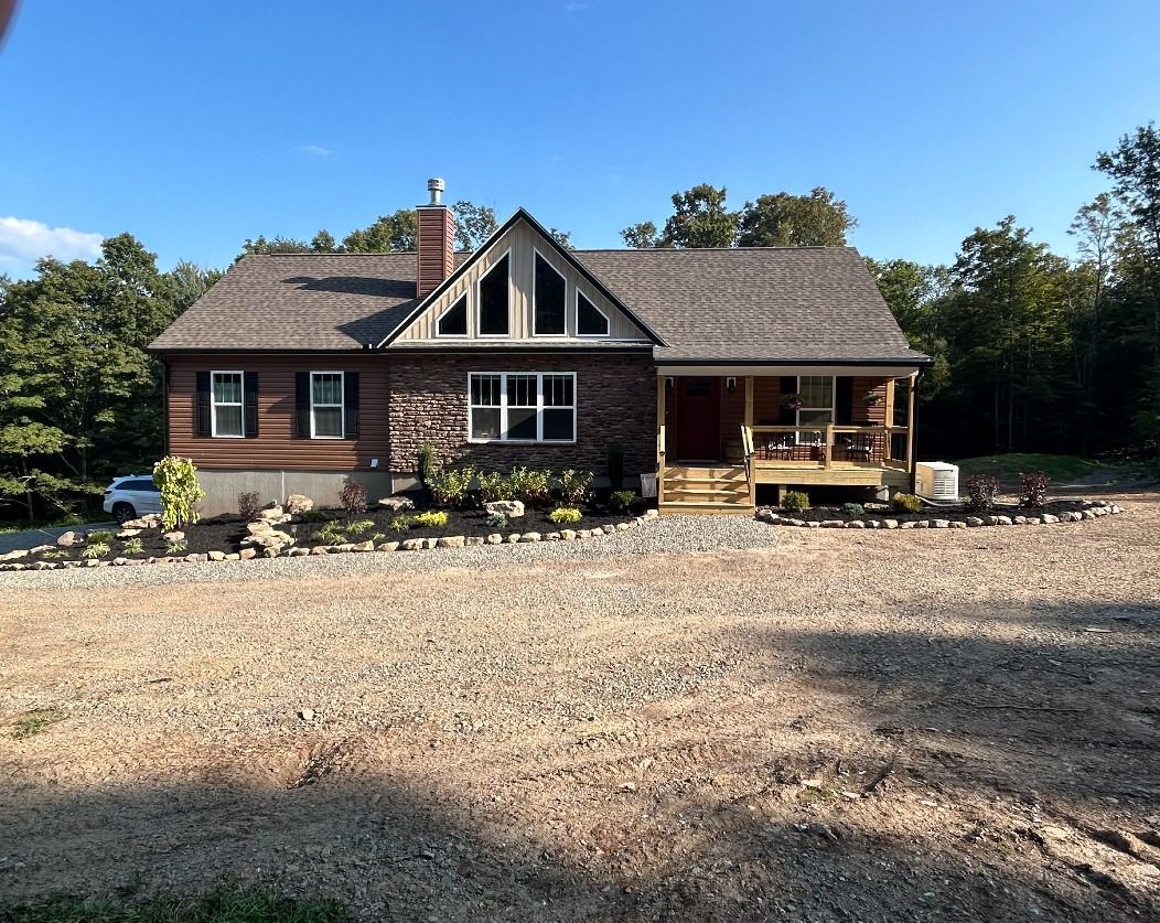 Cabin home with porch, brick and log exterior, surrounded by gravel and trees.