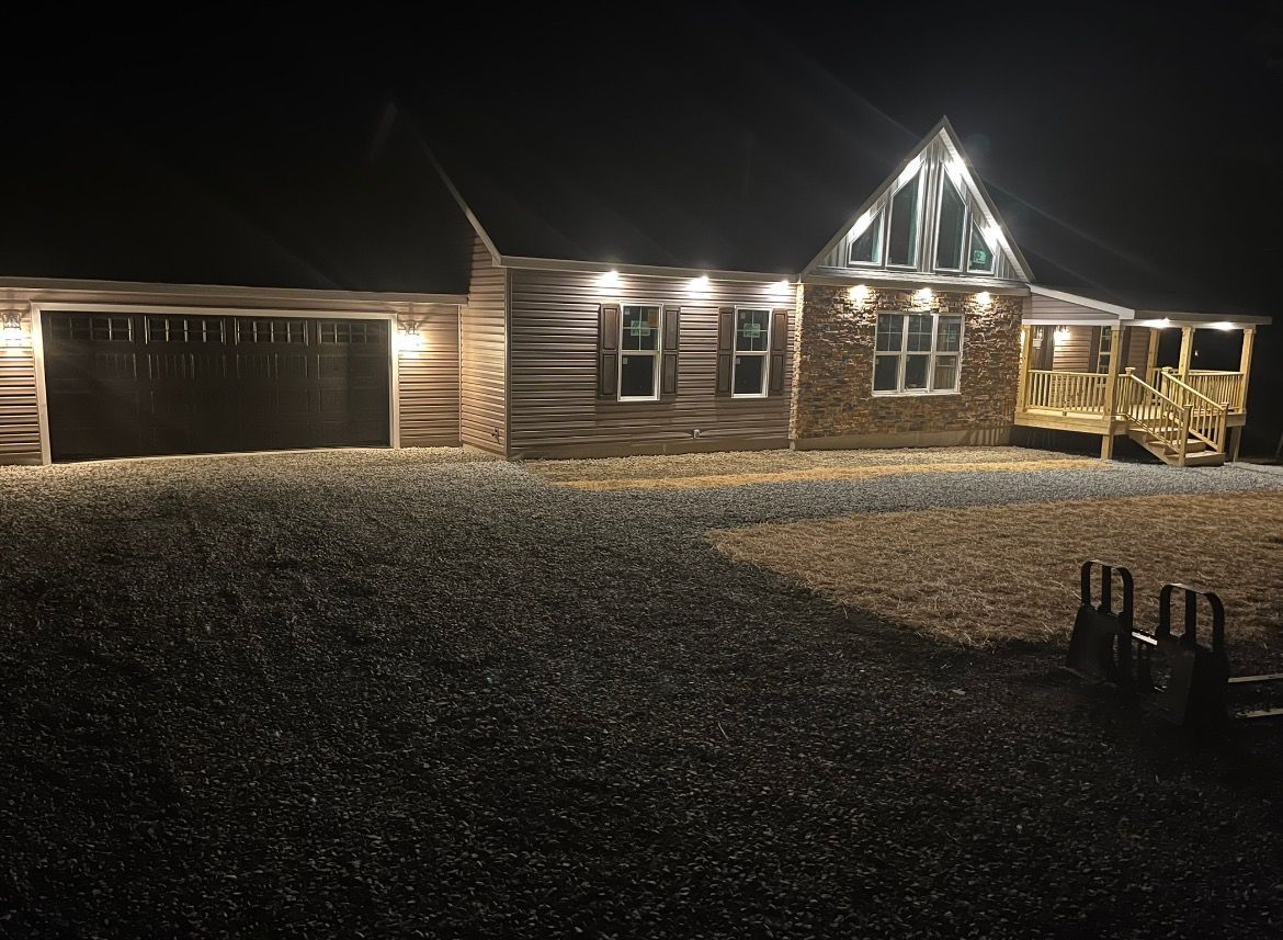 House at night, exterior lit with warm lights, gravel yard, garage, and porch.