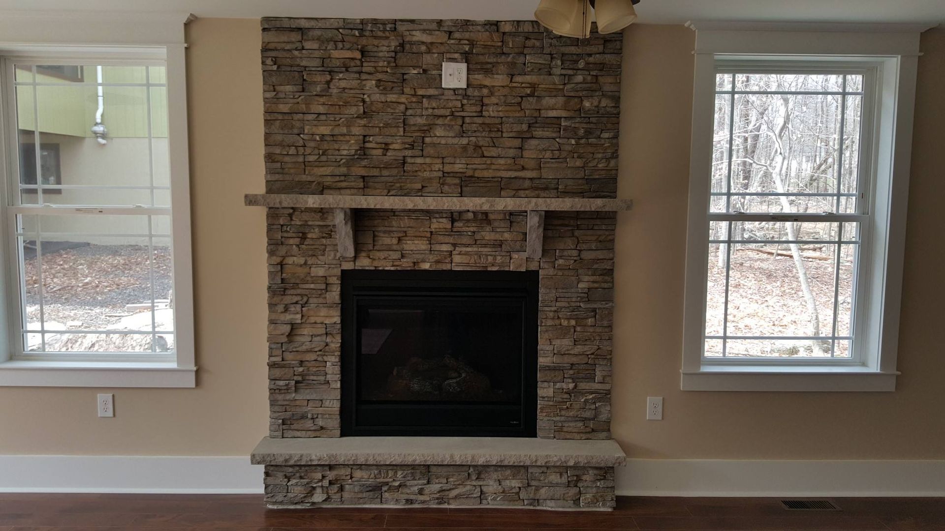 Stone fireplace with black insert, flanked by windows.