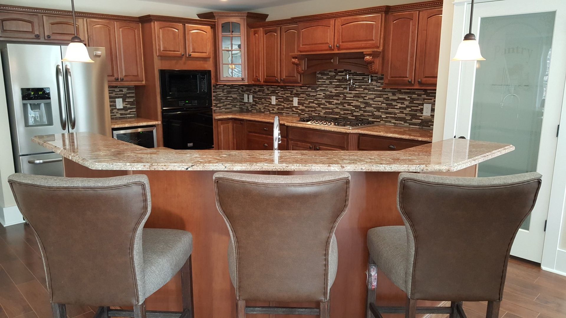 Kitchen with brown cabinets, granite countertops, and three bar stools.