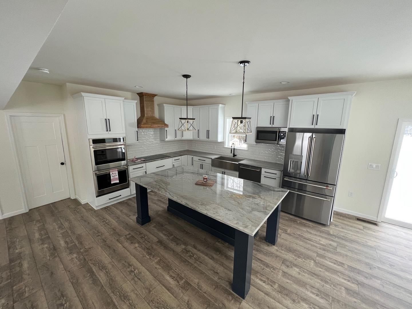 Modern kitchen with white cabinets, dark blue island, and stainless steel appliances.