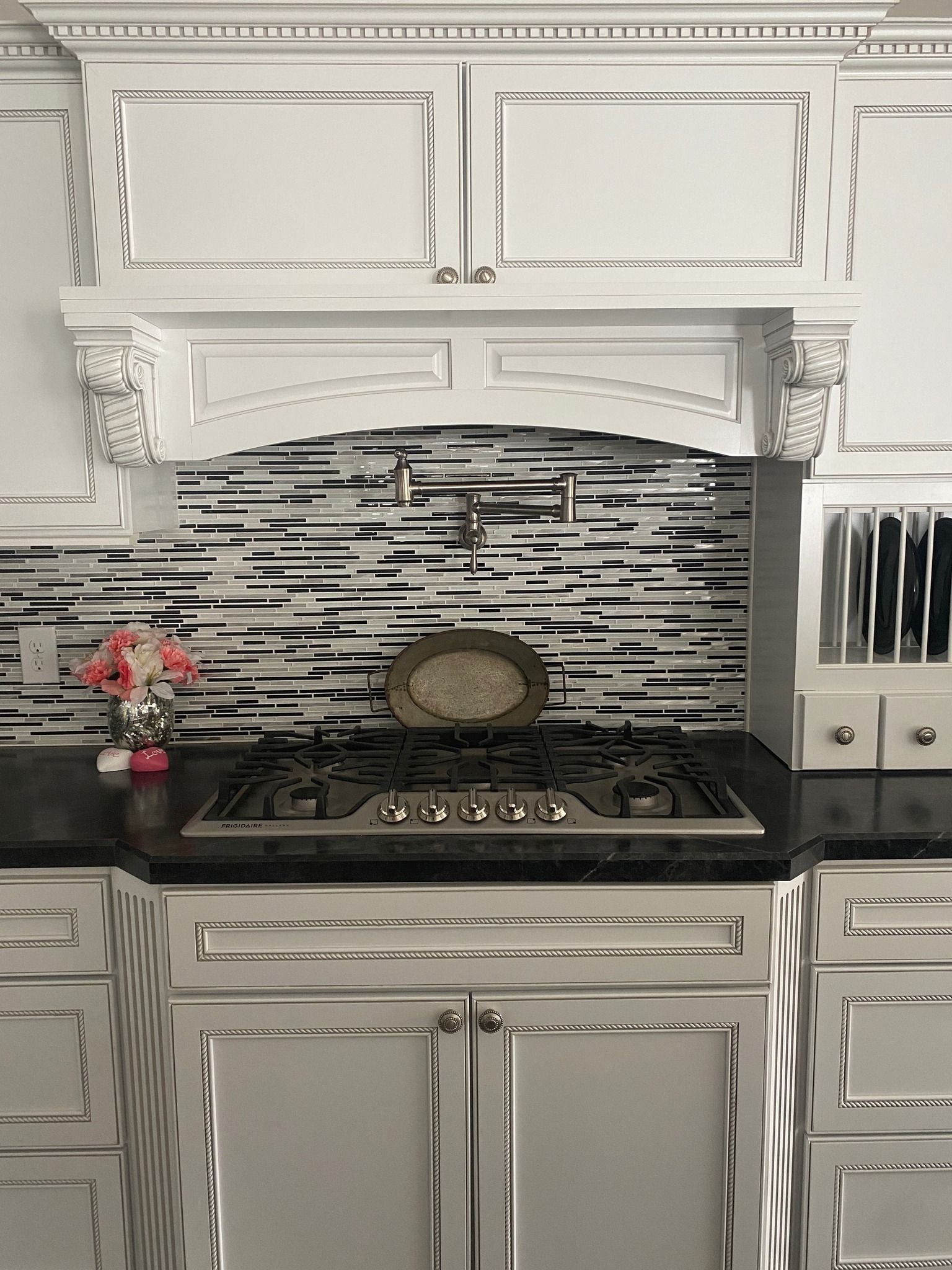 A kitchen stovetop with a metal pot-filler faucet against a black and white horizontal-striped tiled backsplash.