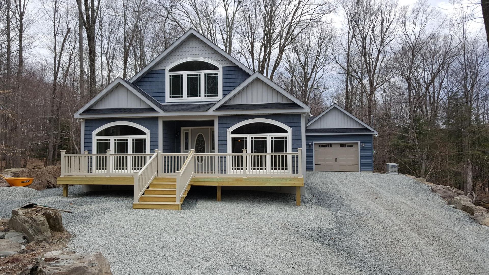 A blue two-story house with a white front deck, light gray accents, arched windows, and an attached garage.