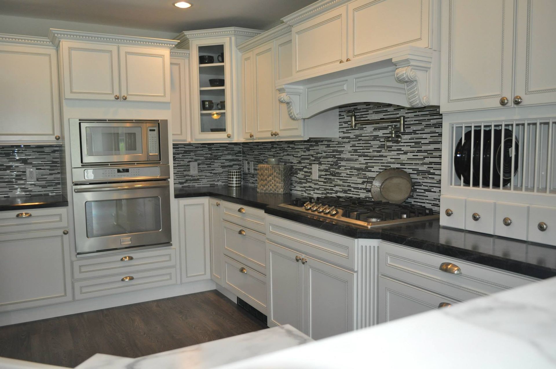 A white kitchen featuring cabinets, black countertops, a stove, double wall ovens, and a decorative tile backsplash.