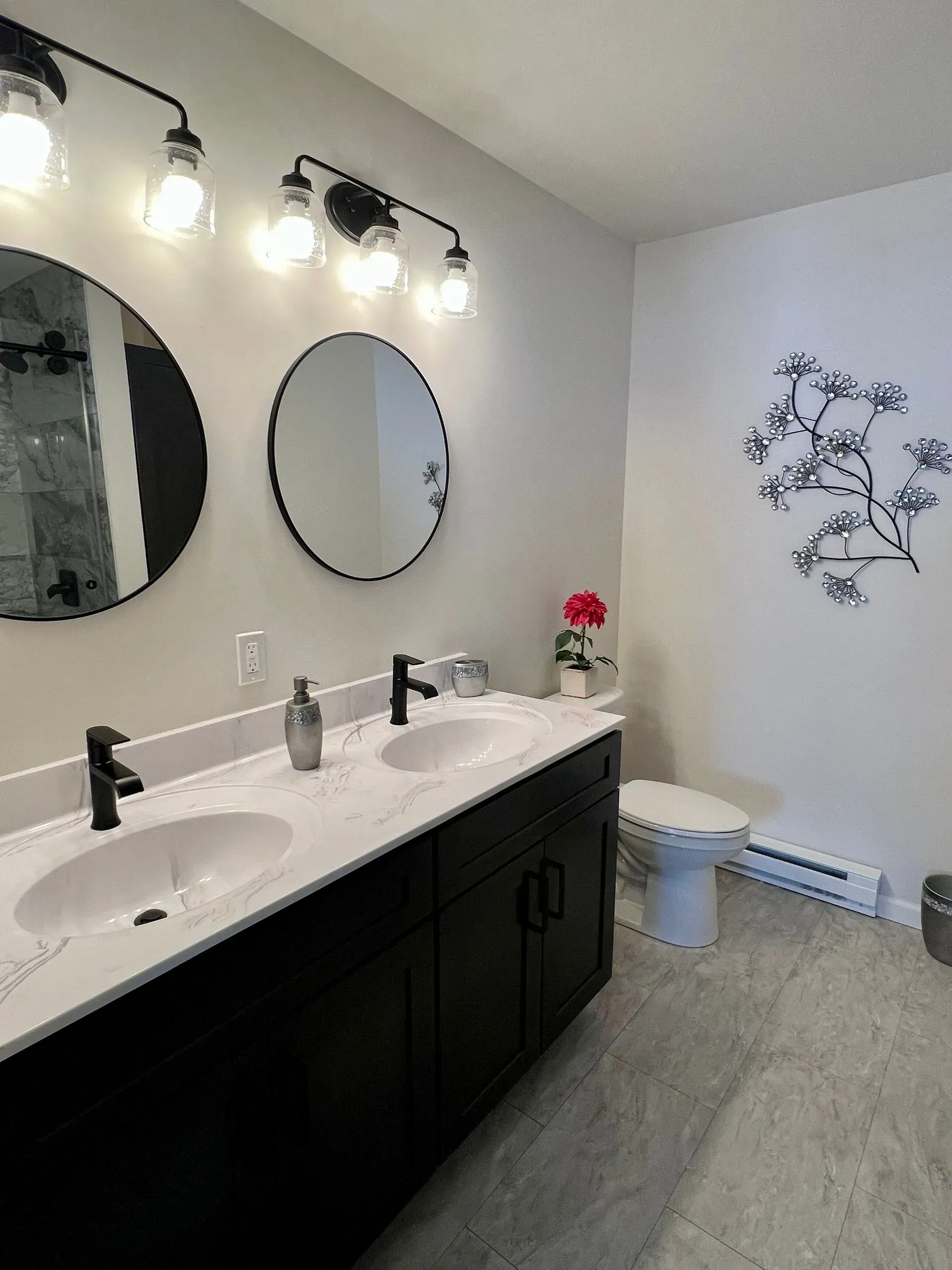 Modern bathroom featuring a double vanity with dark cabinets, two round mirrors, dual sinks, and wall-mounted art.