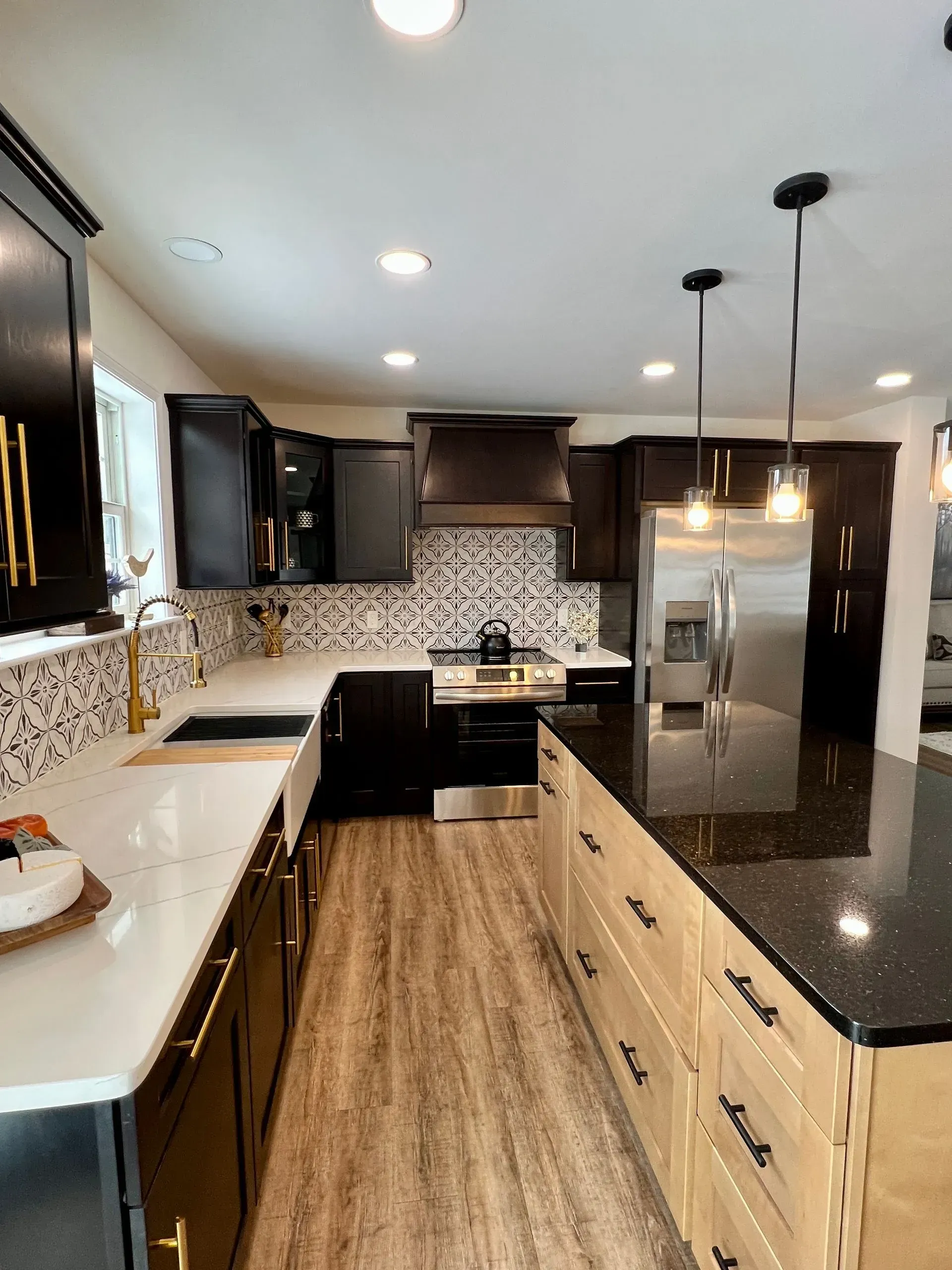 A modern kitchen featuring dark upper cabinets, a light wood kitchen island, white countertops, and a patterned backsplash.