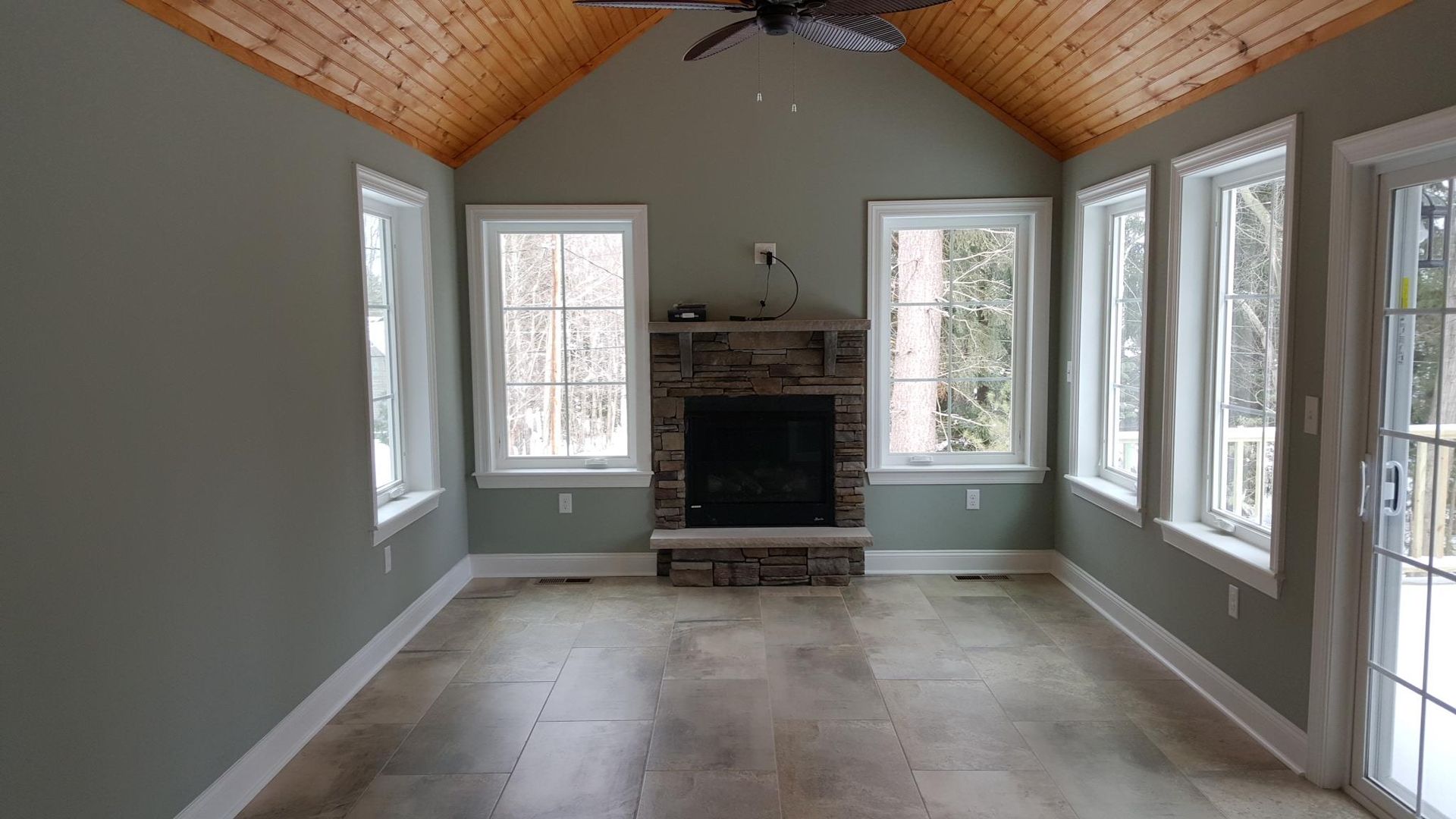 Sunroom interior with fireplace, windows, light wood ceiling, and neutral walls.