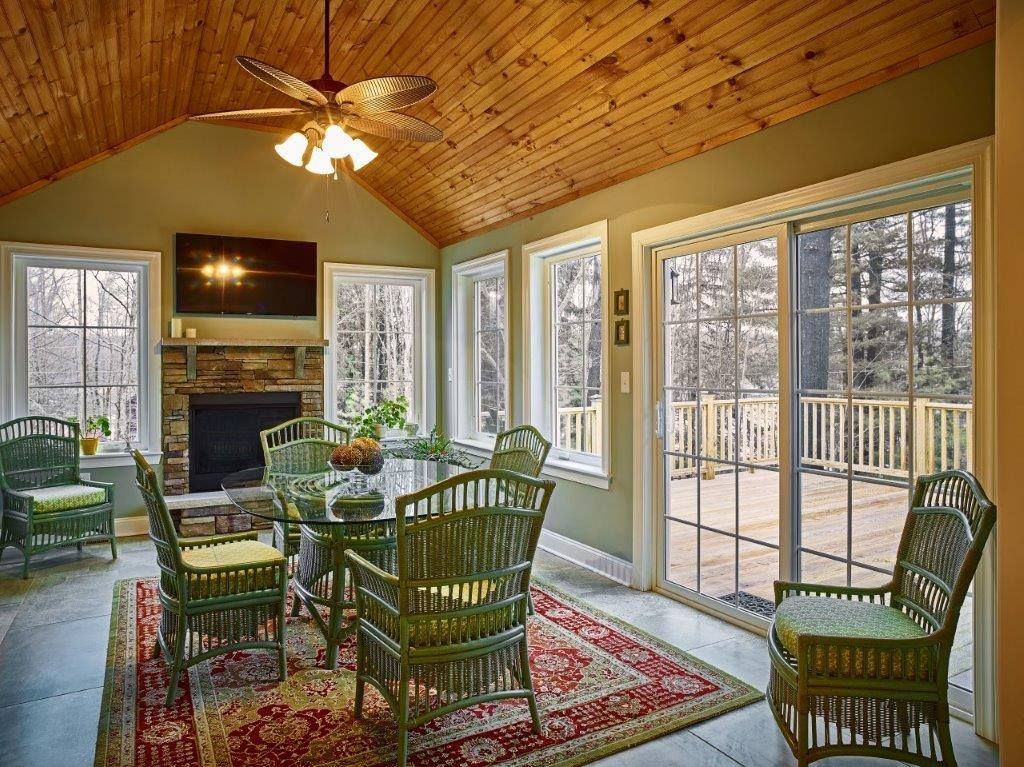 Sunroom with a vaulted wooden ceiling, green wicker furniture on a patterned rug, a stone fireplace, and a sliding door.