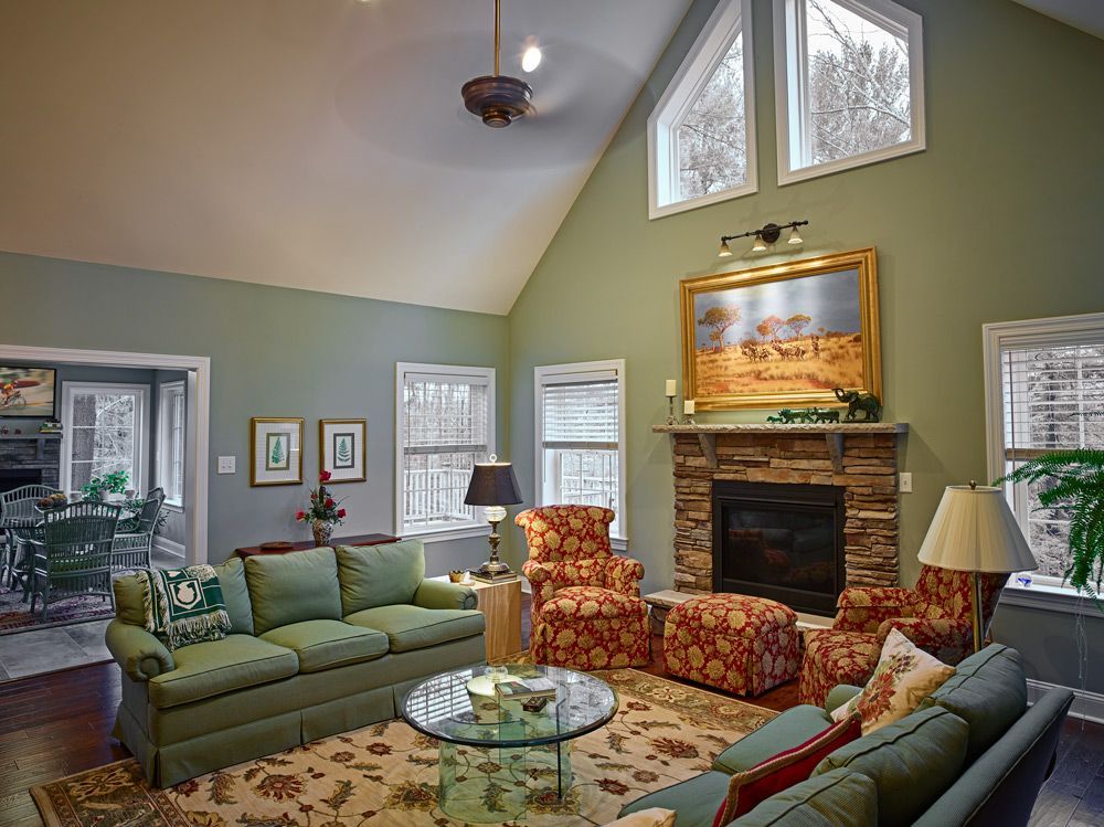 A cozy living room with a stone fireplace, green sofas, floral patterned armchairs, and vaulted ceilings.