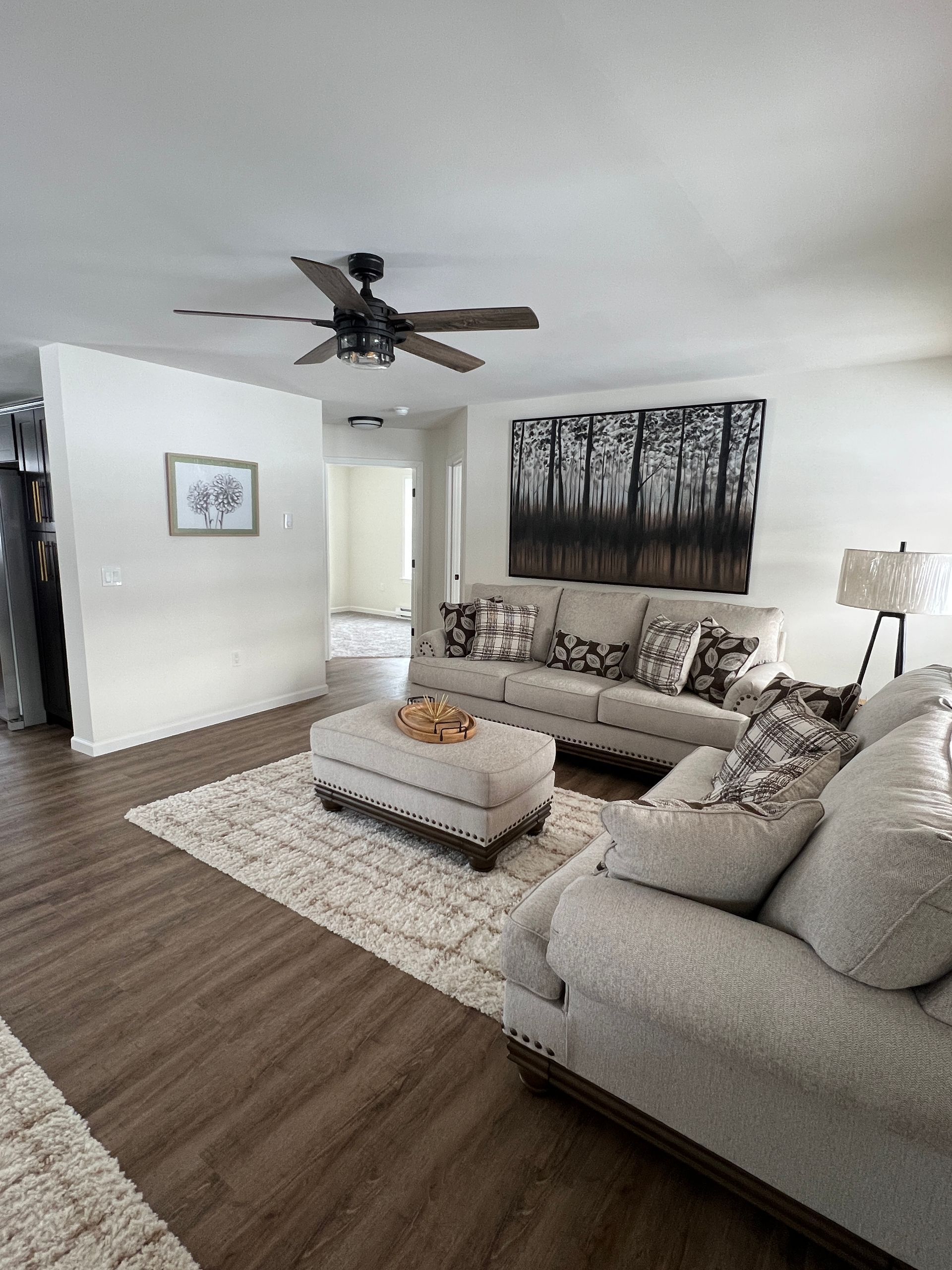 Living room with beige furniture, a rug, dark flooring, and a forest art piece on the wall.