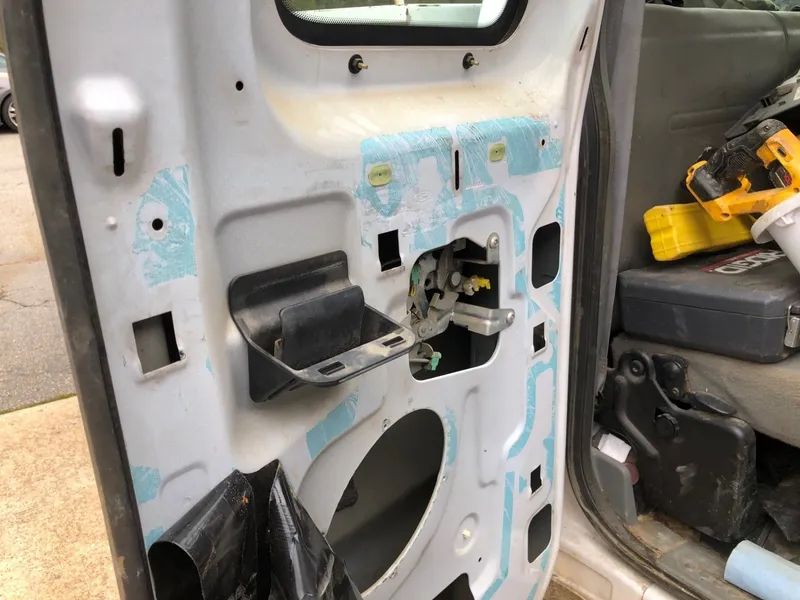 Open car door interior, showing the inner workings, including latch, various components, and a partially removed black protective sheet.