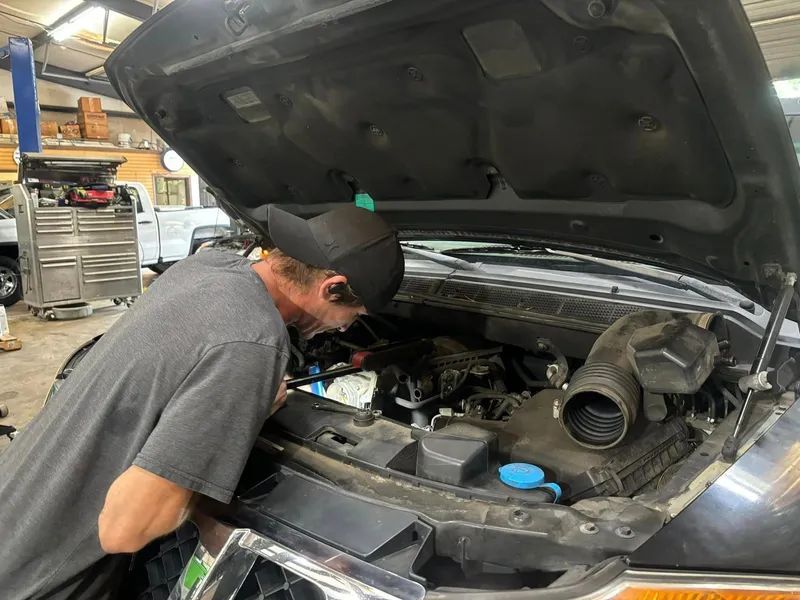 Mechanic inspecting the engine of a vehicle with the hood open in a garage.