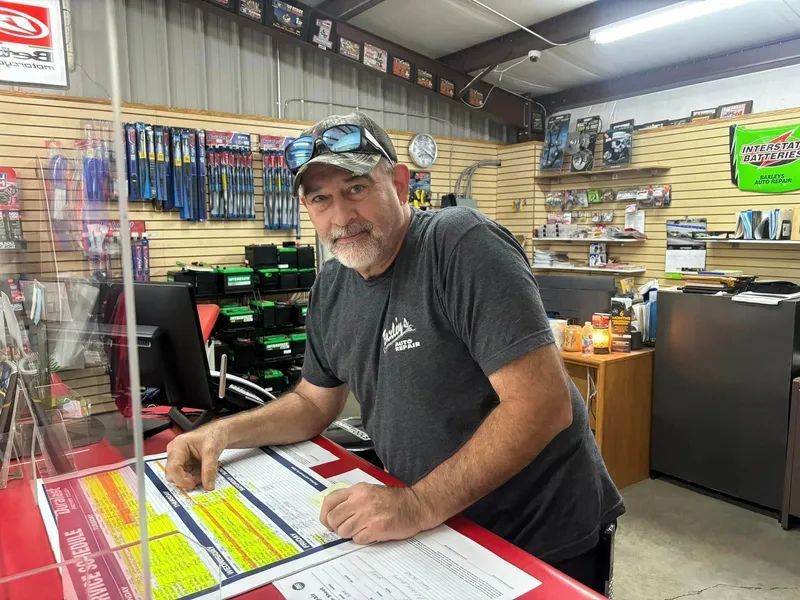 Man leans on counter in store, looking at paperwork. A clear barrier and products are visible.