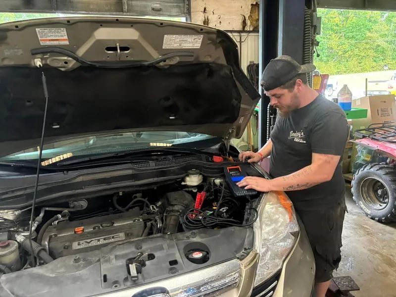 Mechanic working on car engine in a garage; he is using a diagnostic tool.