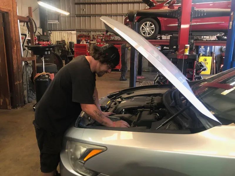 Mechanic working on a car in a garage with the hood open.